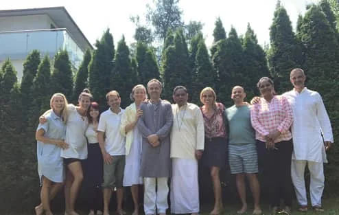 A group of retreat participants standing together outdoors in front of tall green hedges